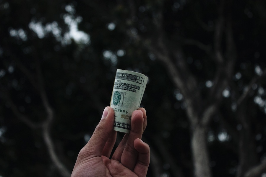 man holding a roll of twenty dollar bills