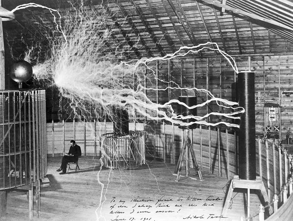 Tesla sitting next to his magnifying transmitter generating millions of volts