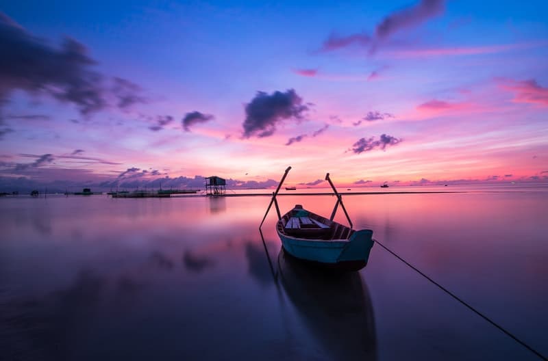 Docked wooden boat on a lake with purple skies behind it