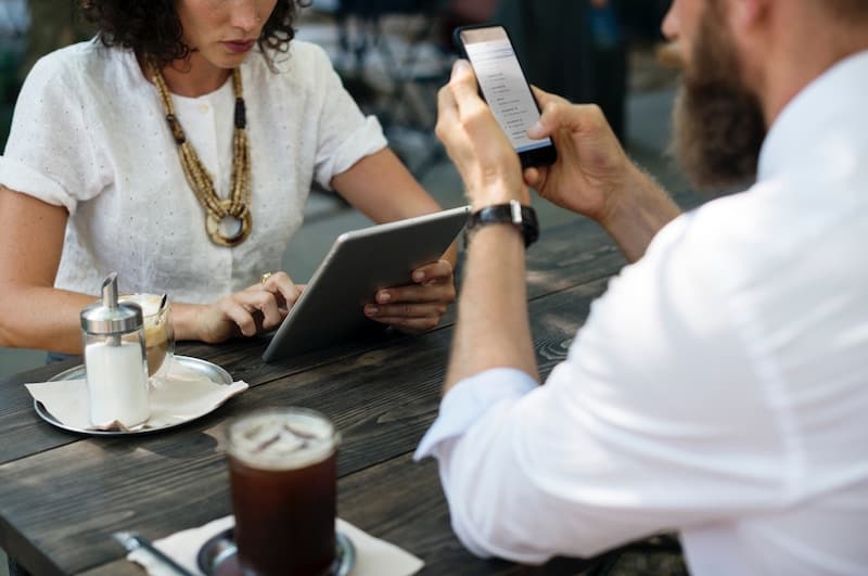 Two coworkers using mobile devices while sitting together