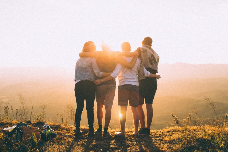 four friends watching the sunset together from a tall mountain