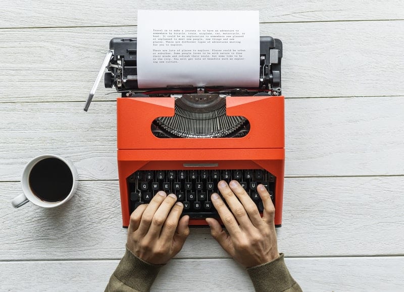 person typing on a vintage black and orange typewriter