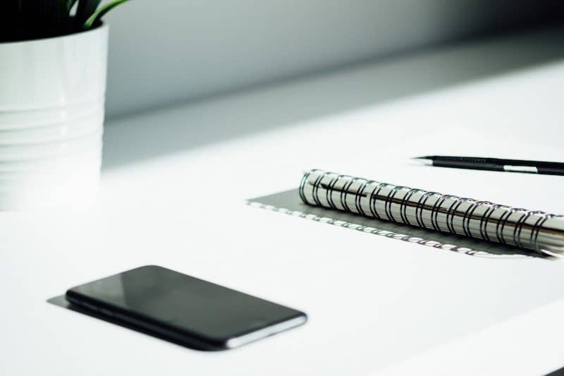 Iphone and a notepad laying on top of a white office desk