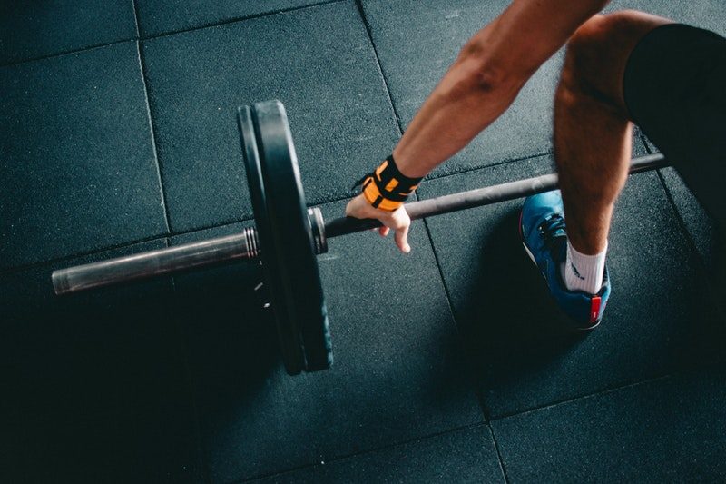 Person Wearing Black Shorts and Blue Lace-up Low-top Sneaker holding a Black Barbell