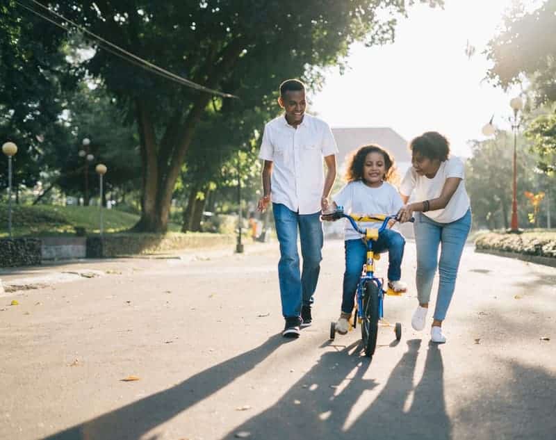 family teaching their daughter how to ride a bicycle-min