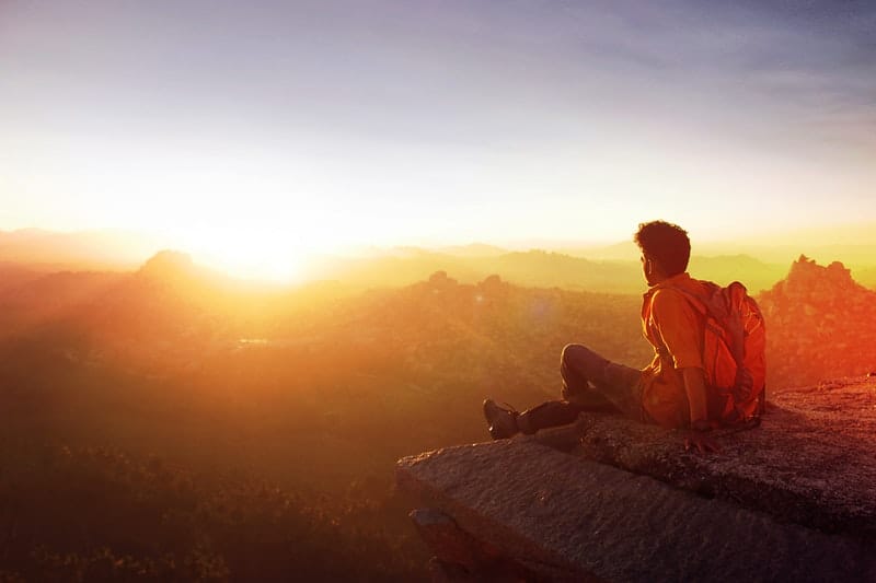 man sitting on the edge of a rock watching the sunrise