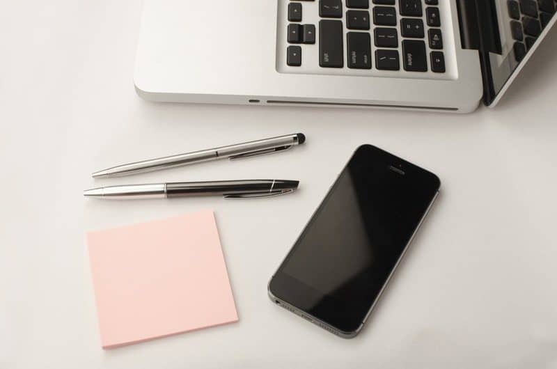 notepad pens and iphone laying on top of a white table next to a macbook pro