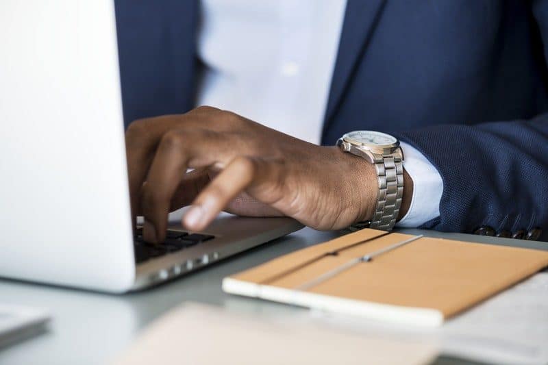 Photo of Person Wearing Gray Analog Watch Typping on a laptop Keyboard