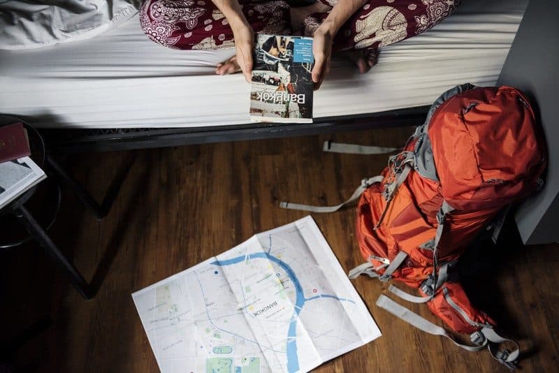 backpacker staying inside a hostel reading lonely planet guide book about bangkok thailand