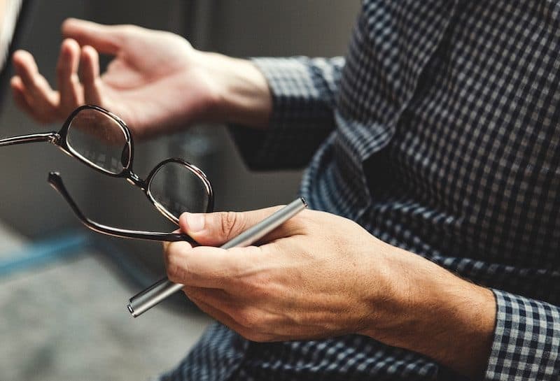 Man Holding his reading glasses while talking