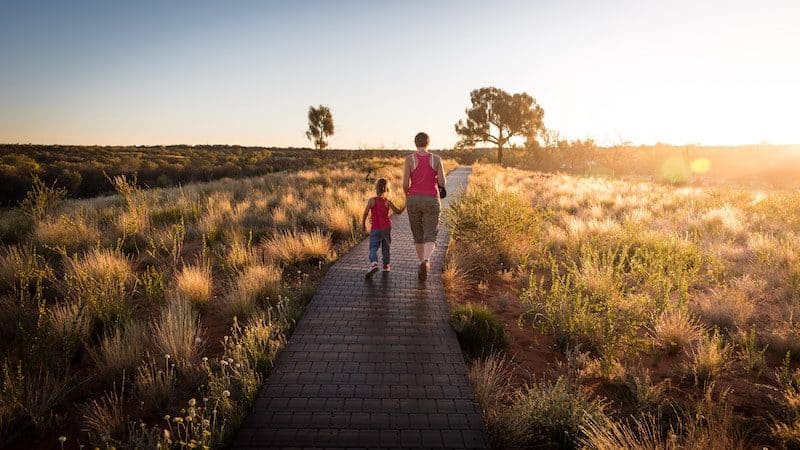 mother and daughter walking on a wooden path into the sunset