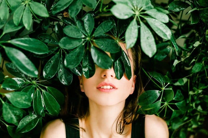 woman hiding her eyes behind a green plant