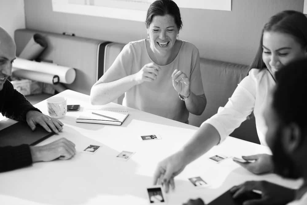 grayscale photo of two men and two women playing cards on table white laughing