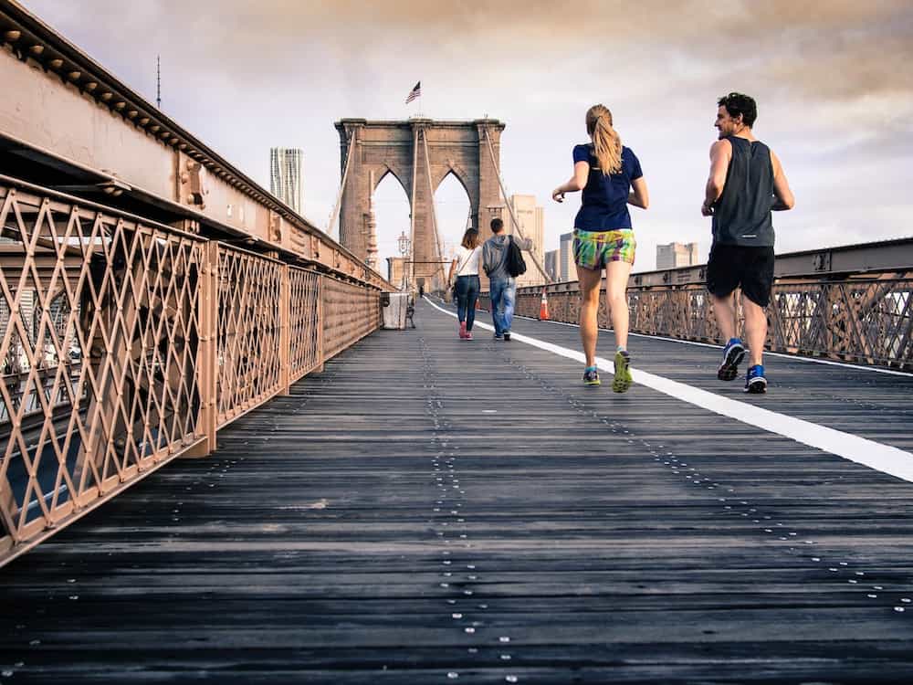 man and woman in black tops jogging at bridge under clear skies