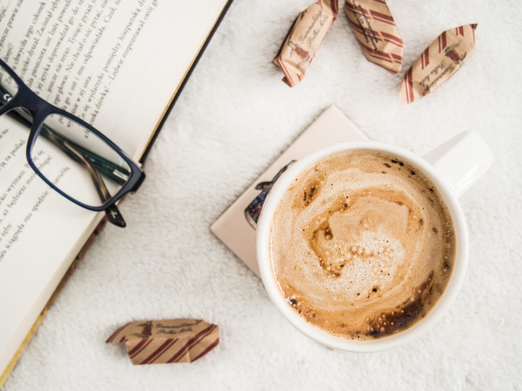 Coffee cup, book, and glasses on a table. 