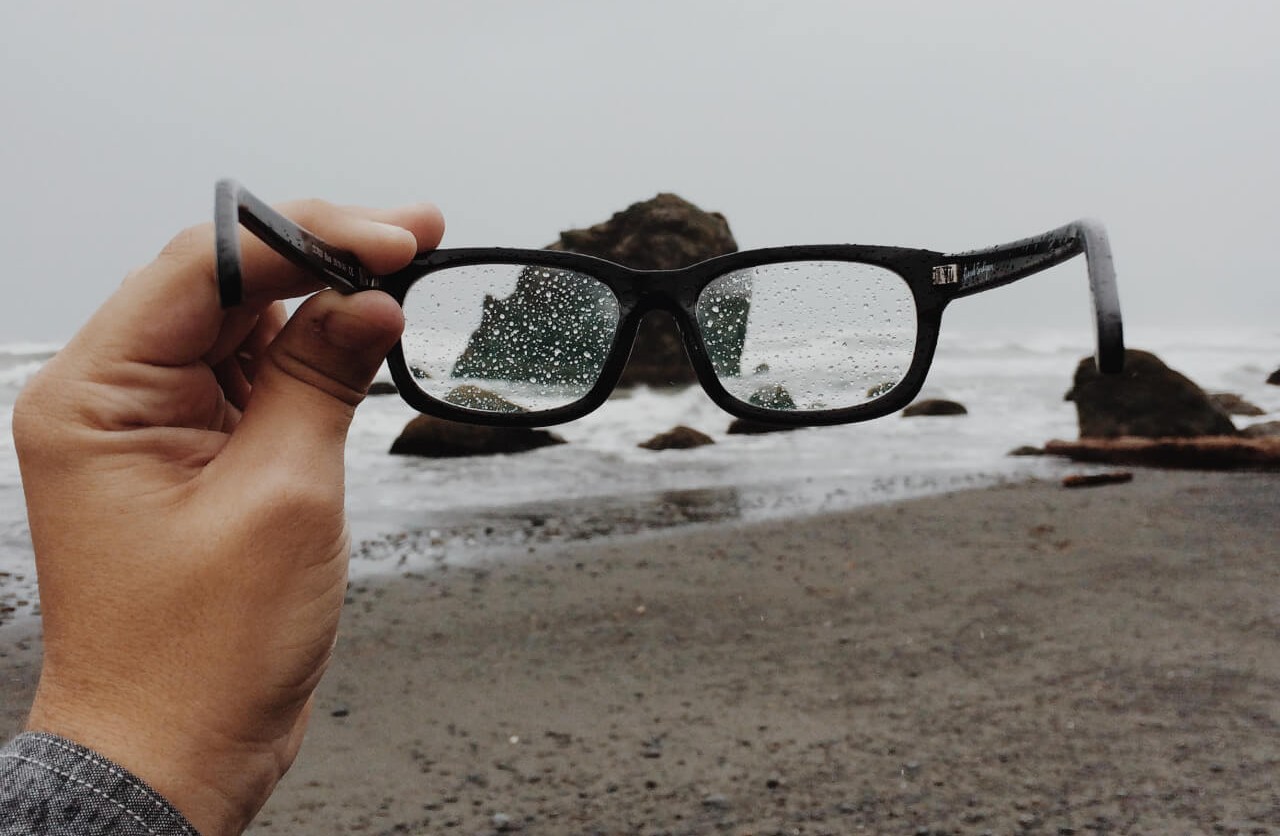 Man holding his glasses while its raining.