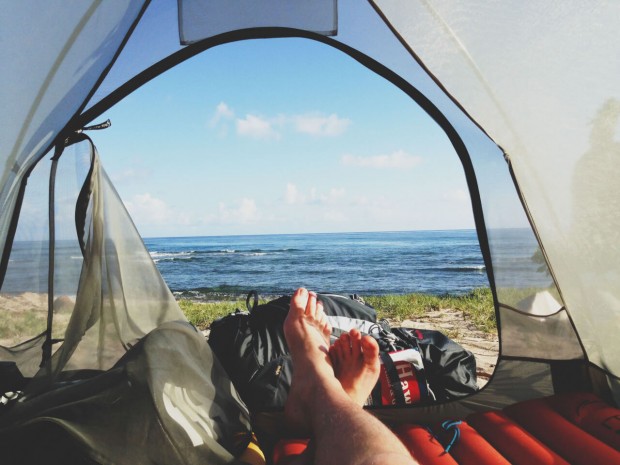 Man waking up inside a tent that overlooks a beach.