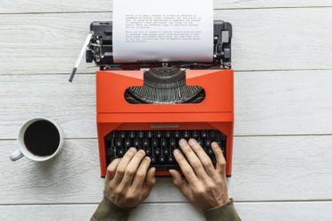 Man typing on a red vintage typewriter-min