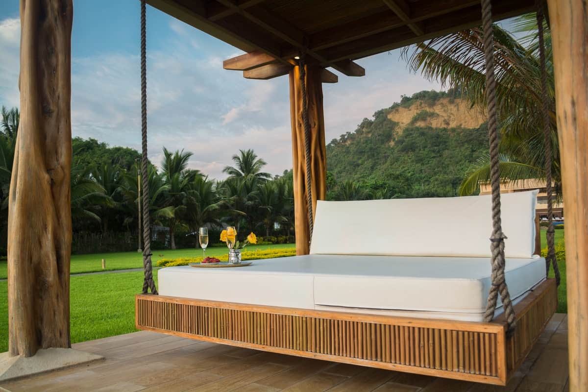 brown wooden framed white mattress hanging bed surrounded by green grass