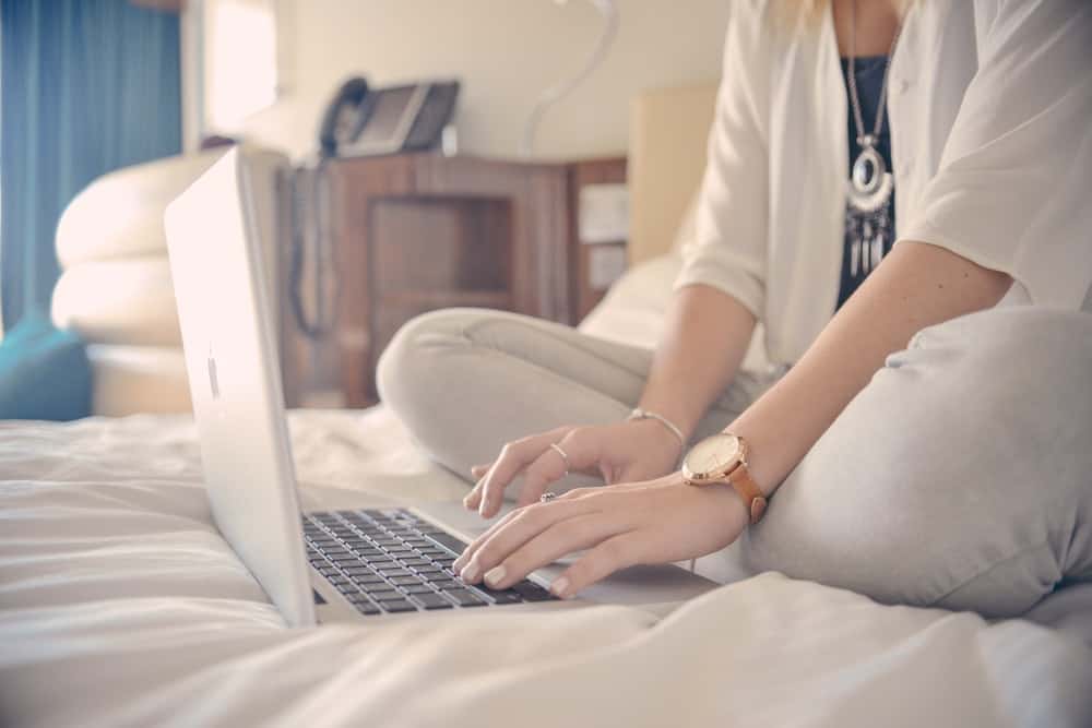 woman typing on her laptop while sitting on the bed