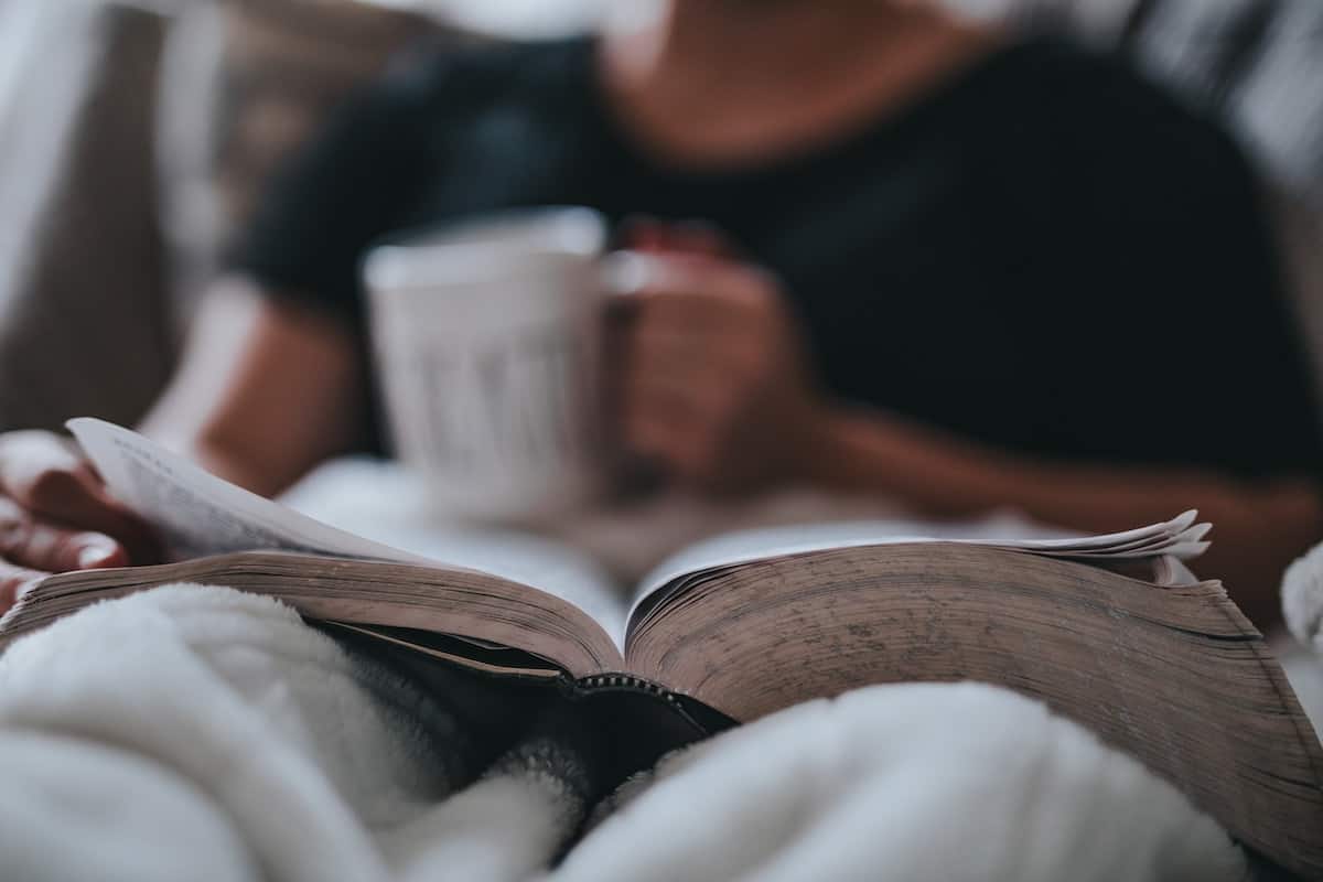 Man reading a book while drinking coffee in his bed