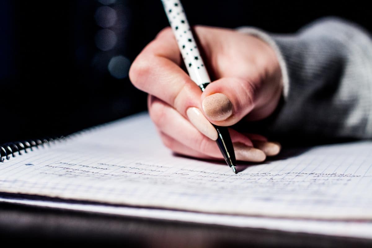 woman using a pen to write an essay in her notebook