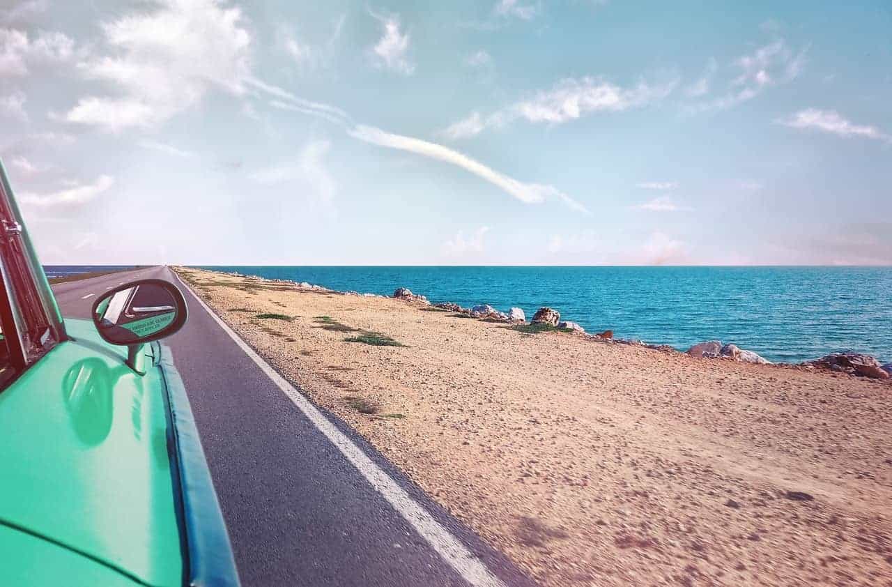 green car near seashore with blue ocean