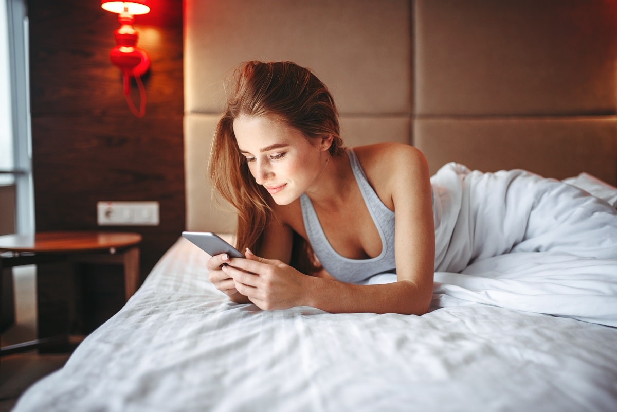 Attractive woman lies in bed and using phone