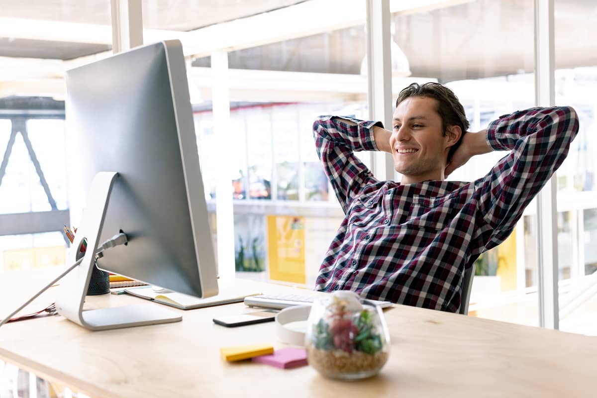 Happy Caucasian male graphic designer with hands behind head sitting on chair in a modern office