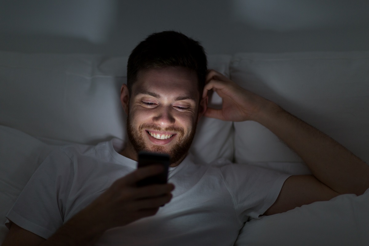 happy young man with smartphone in bed at night