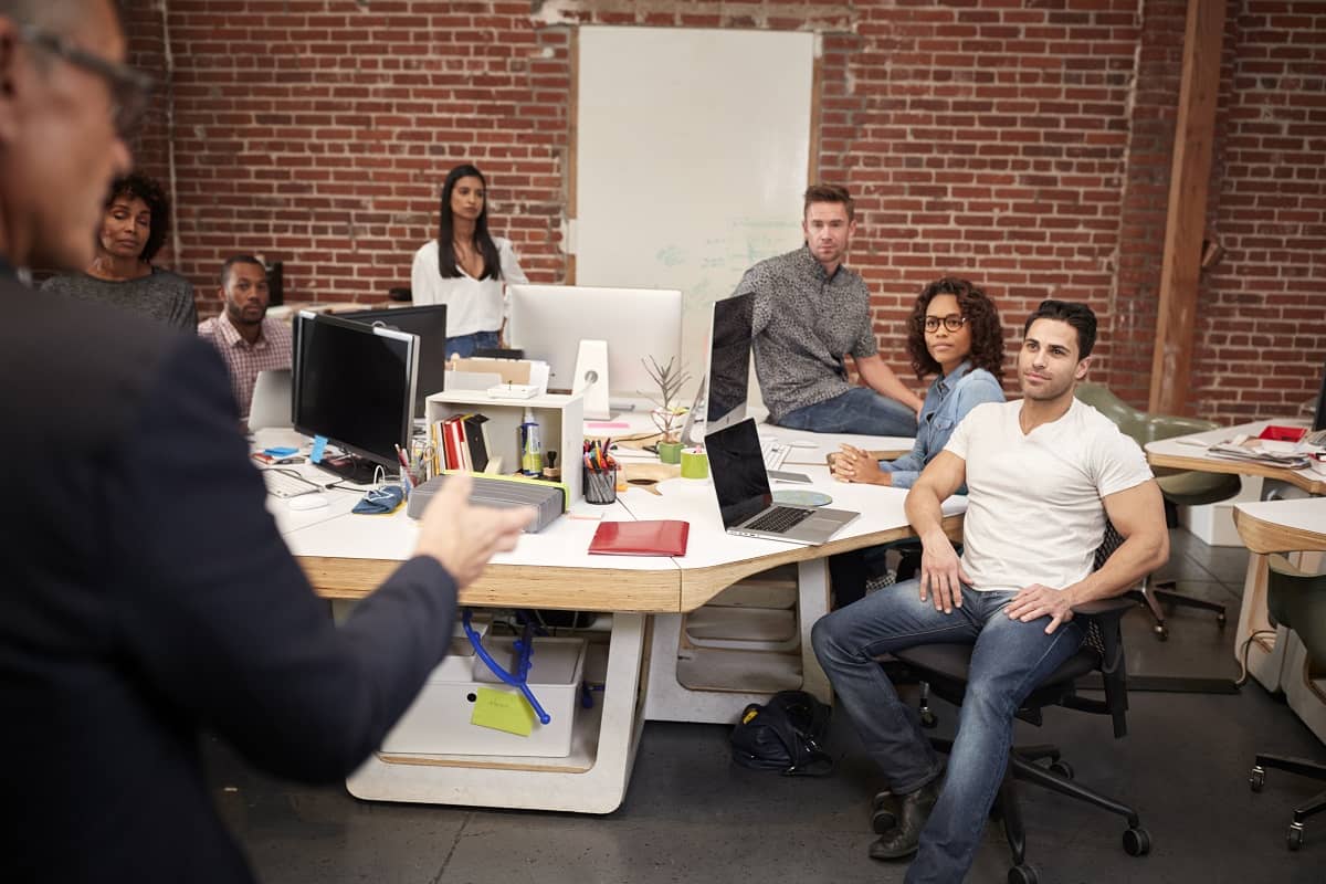 Senior Businessman Talking At Meeting Of Casually Dressed Business Team In Open Plan Office