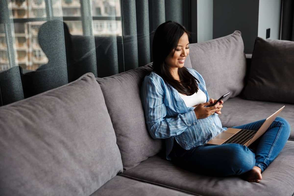 Photo of smiling pregnant asian woman using laptop and mobile phone