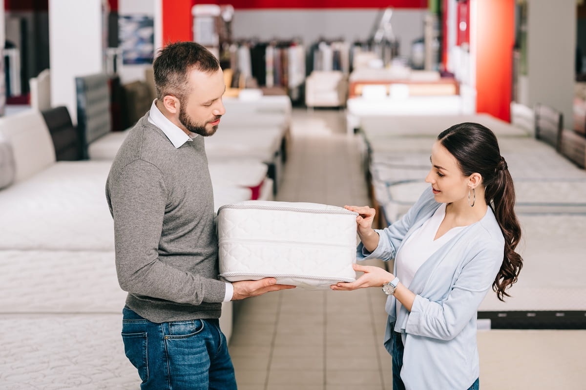 couple choosing folding mattress together in furniture store with arranged mattresses