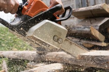 Male hands sawing old boards for firewood with a professional chainsaw