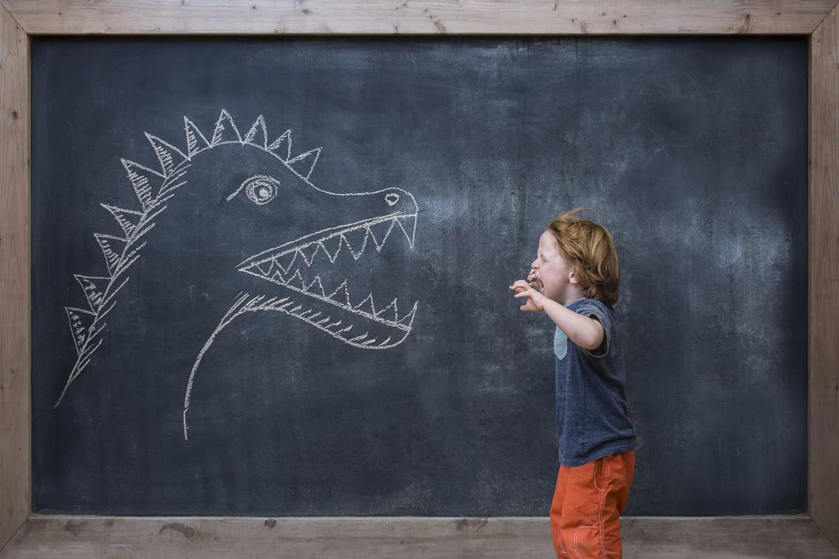 Young boy roaring at dinosaur drawing on blackboard